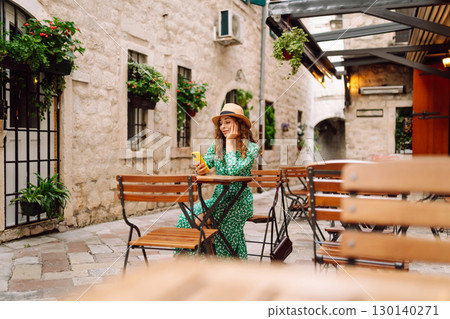 Young woman holding a smartphone digital camera with her hands while sitting at the summer cafe 130140271