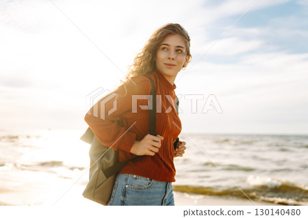 As she walked along the beach, the woman tourist adjusted her backpack, taking in the salty sea air As she walked along the beach, the woman tourist adjusted her backpack, taking in the salty sea air 130140480