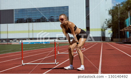 Female hurdler bending with exhaustion after intensive training on track 130140492