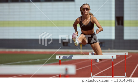 Female hurdler mid-jump over barrier symbolizing courage and determination in sport 130140495