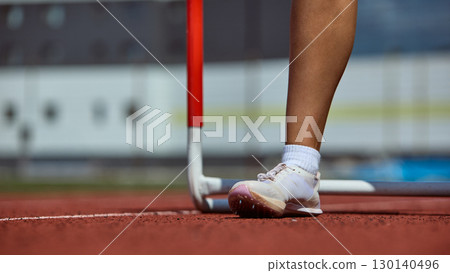 Detail of runner foot near hurdle on stadium track symbolizing first step to victory Detail of runner foot near hurdle on stadium track symbolizing first step to victory 130140496