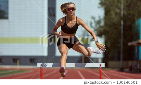 Overhead view of female hurdler jumping obstacle on red athletics track with shadow Overhead view of female hurdler jumping obstacle on red athletics track with shadow 130140501