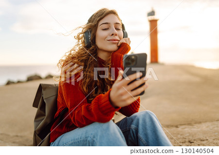 Happy woman listening nice music by the waterfront while wearing headphones by a lighthouse. 130140504