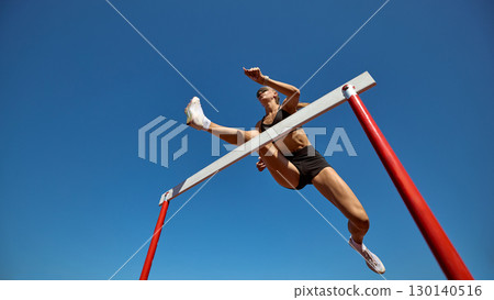 Female hurdler in low angle action leap against clear sky 130140516