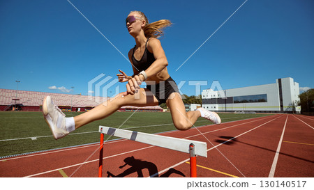 Young female athlete hurdling with speed and focus on outdoor track 130140517