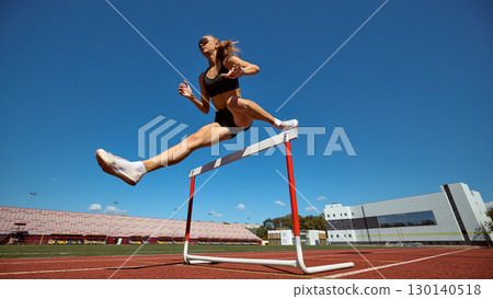 Female hurdler mid-air over hurdle with dynamic stride on stadium track 130140518