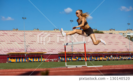 Strong woman athlete in flight above hurdle during stadium race 130140520