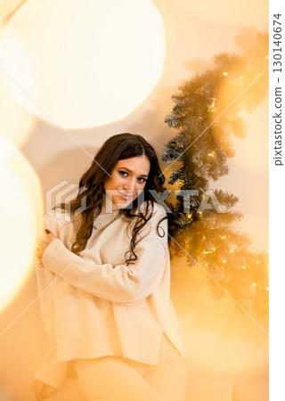 Woman in Cream Sweater Standing by Decorated Tree 130140674