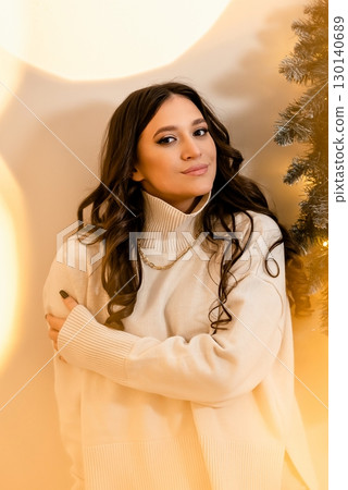 Woman in Cozy Sweater Posing by Christmas Tree Woman in Cozy Sweater Posing by Christmas Tree 130140689