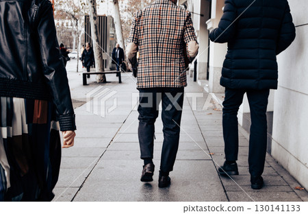 Stylish people walk down a city sidewalk on a cold day, showcasing fashion on a city sidewalk. Urban lifestyle. Walking people on the urban street. Stylish people walk down a city sidewalk on a cold day, showcasing fashion on a city sidewalk. Urban lifestyle. Walking people on the urban street. 130141133