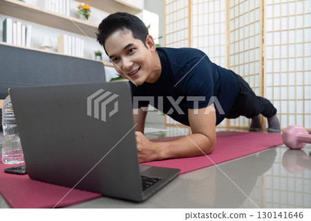 Man performing plank exercise while using laptop at home 130141646