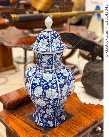 Porcelain vase with lid decorated with blue floral ornament standing on wooden table. Traditional craft, antique design, cultural heritage and decorative interior object. Porcelain vase with lid decorated with blue floral ornament standing on wooden table. Traditional craft, antique design, cultural heritage and decorative interior object. 130142049