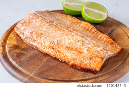 Baked salmon fillet paired with fresh lime halves on rustic wooden cutting board Baked salmon fillet paired with fresh lime halves on rustic wooden cutting board 130142543