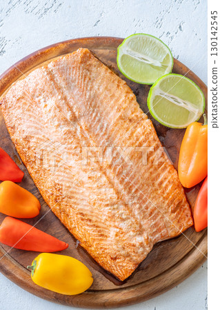 Colorful peppers and lime enhance baked salmon fillet on rustic wooden cutting board Colorful peppers and lime enhance baked salmon fillet on rustic wooden cutting board 130142545