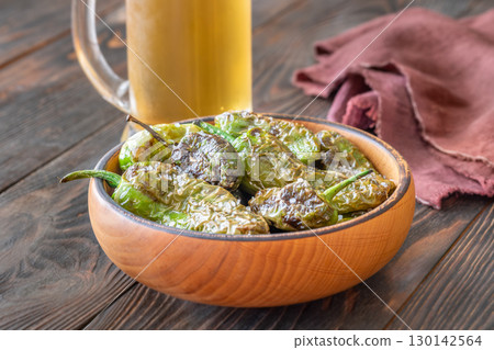 Terracotta bowl of Pimientos de Padron served with cold frothy beer 130142564
