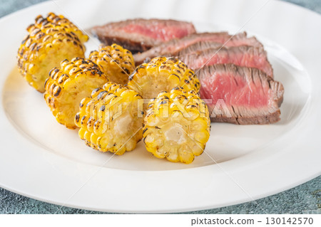 Juicy medium rare beef steak with roasted golden corn on white plate 130142570