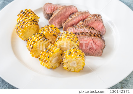 Juicy medium rare beef steak with roasted golden corn on white plate 130142571