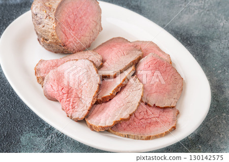Perfectly sliced roast beef medium rare with seared crust on white plate 130142575