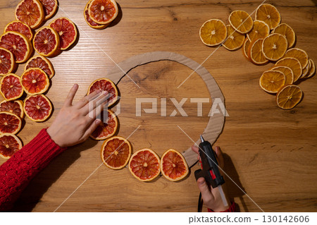 Woman using hot glue Handmade Christmas wreath from dried orange grapefruit slices. Festive holiday preparation craft master class of creative making decor. Hands-on activities sustainable responsible Woman using hot glue Handmade Christmas wreath from dried orange grapefruit slices. Festive holiday preparation craft master class of creative making decor. Hands-on activities sustainable responsible 130142606