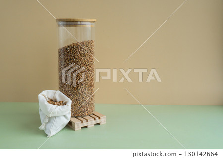 Refillable glass jar with raw buckwheat porridge and cotton bag. Copy space Refill product format eco-friendly living. Filling reusable container Whole spelt grain species. High protein fiber-rich Refillable glass jar with raw buckwheat porridge and cotton bag. Copy space Refill product format eco-friendly living. Filling reusable container Whole spelt grain species. High protein fiber-rich 130142664