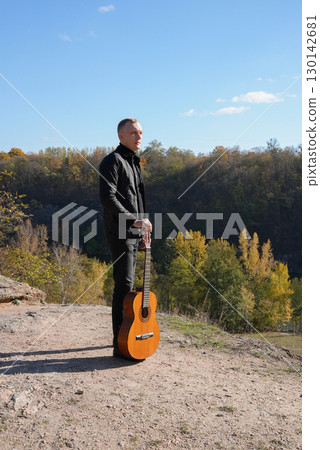Portrait of smiling caucasian artist plays wooden acoustic guitar in autumnal park. Young songwriter plays string musical instrument hobby outside in nature fall time. Audio music healing Portrait of smiling caucasian artist plays wooden acoustic guitar in autumnal park. Young songwriter plays string musical instrument hobby outside in nature fall time. Audio music healing 130142681