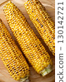 Three grilled corn cobs with char marks resting on wooden cutting board 130142721