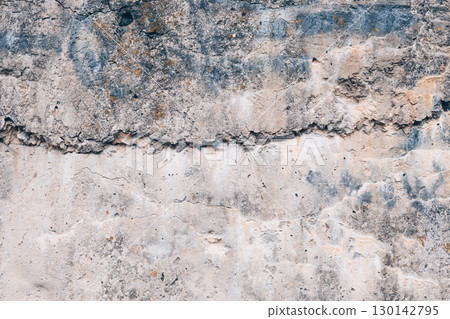 A fragment of the rough texture of an old concrete surface with cracks, stains and layers of weathered material. Gray-beige shade, pronounced relief and wear. Texture of a concrete wall. 130142795