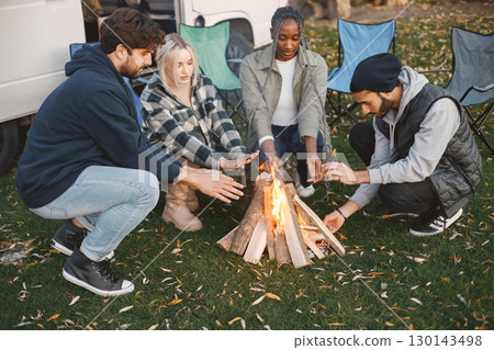 Multi racial friends having out of city picnic. They made a fire and sitting aroud warming hands. European, black, pakistani race. Travelling with van. Multi racial friends having out of city picnic. They made a fire and sitting aroud warming hands. European, black, pakistani race. Travelling with van. 130143498