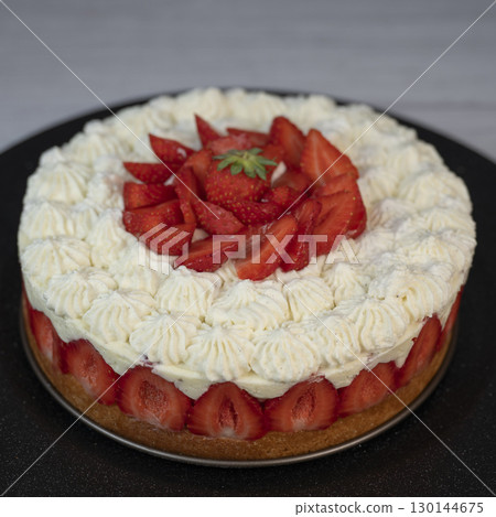 Delightful fraisier cake topped with fresh strawberries and whipped cream is served at a gathering 130144675