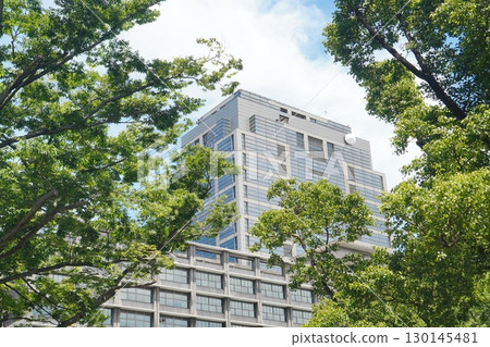 現代化高層辦公大樓外觀,周圍環繞著藍天、清新綠樹和城市風光 現代化高層辦公大樓外觀,周圍環繞著藍天、清新綠樹和城市風光 130145481