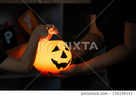 Halloween. Child and adult exchanging glowing pumpkin bucket. Halloween. Child and adult exchanging glowing pumpkin bucket. 130146141