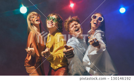 Group of friends in retro disco outfits performing playful poses under colorful lights Group of friends in retro disco outfits performing playful poses under colorful lights 130146192