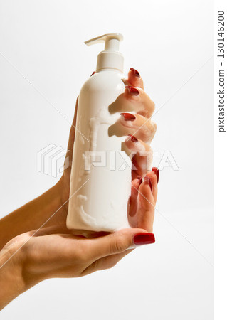 Female hands holding cosmetic pump bottle with foam against white background Female hands holding cosmetic pump bottle with foam against white background 130146200
