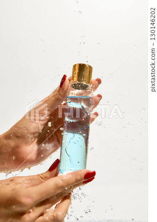 Female hands holding transparent cosmetic toner bottle under falling water Female hands holding transparent cosmetic toner bottle under falling water 130146202