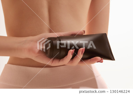 Black cosmetic tube in woman hand against bare back closeup 130146224