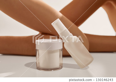 White cream jar and spray bottle on table near crossed legs of woman closeup White cream jar and spray bottle on table near crossed legs of woman closeup 130146243