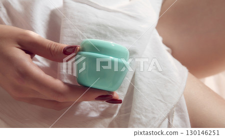 Female hand holding turquoise cosmetic cream jar on soft fabric background 130146251