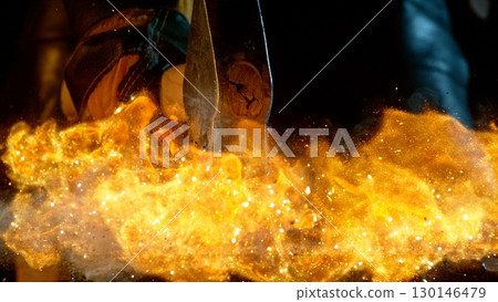 The blacksmith manually forging the molten metal on the anvil in smithy with spark fireworks 130146479