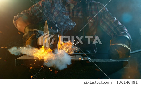 The blacksmith manually forging the molten metal on the anvil in smithy with spark fireworks The blacksmith manually forging the molten metal on the anvil in smithy with spark fireworks 130146481
