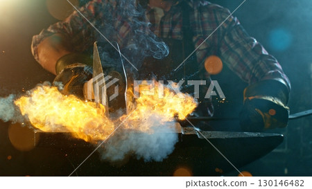 The blacksmith manually forging the molten metal on the anvil in smithy with spark fireworks The blacksmith manually forging the molten metal on the anvil in smithy with spark fireworks 130146482