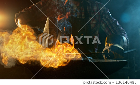 The blacksmith manually forging the molten metal on the anvil in smithy with spark fireworks The blacksmith manually forging the molten metal on the anvil in smithy with spark fireworks 130146483