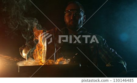 The blacksmith manually forging the molten metal on the anvil in smithy with spark fireworks 130146485
