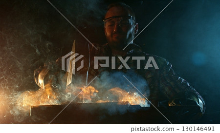 The blacksmith manually forging the molten metal on the anvil in smithy with spark fireworks 130146491
