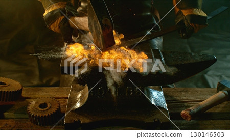 The blacksmith manually forging the molten metal on the anvil in smithy with spark fireworks The blacksmith manually forging the molten metal on the anvil in smithy with spark fireworks 130146503
