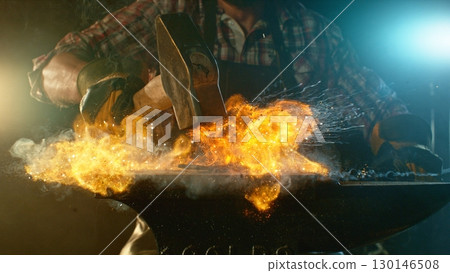 The blacksmith manually forging the molten metal on the anvil in smithy with spark fireworks 130146508