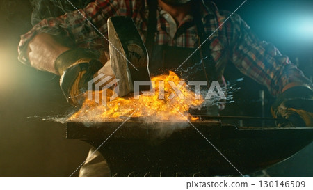 The blacksmith manually forging the molten metal on the anvil in smithy with spark fireworks 130146509