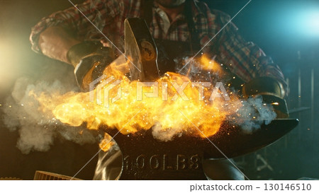 The blacksmith manually forging the molten metal on the anvil in smithy with spark fireworks 130146510
