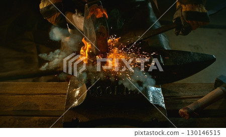 The blacksmith manually forging the molten metal on the anvil in smithy with spark fireworks 130146515