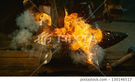 The blacksmith manually forging the molten metal on the anvil in smithy with spark fireworks 130146517