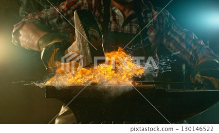 The blacksmith manually forging the molten metal on the anvil in smithy with spark fireworks The blacksmith manually forging the molten metal on the anvil in smithy with spark fireworks 130146522